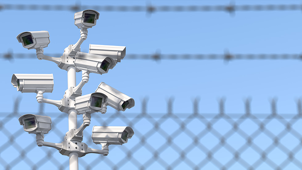 A tower of security cameras with barbed wire in the foreground.